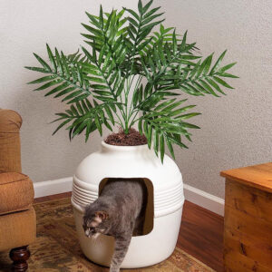 A cat is playing with a potted plant in a living room, near the Good Pet Stuff, The Original Hidden Litter Box - Vented & Odor Filter - Easy to Clean.