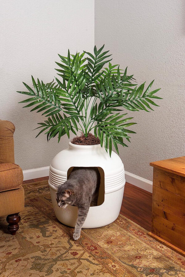 A cat is playing with a potted plant in a living room, near the Good Pet Stuff, The Original Hidden Litter Box - Vented & Odor Filter - Easy to Clean.